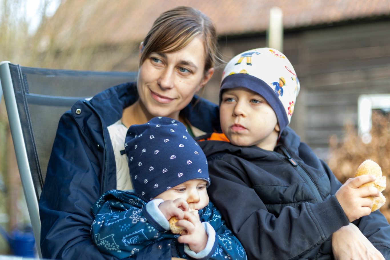 Frau sitzt mit zwei Kindern im Freien und genießt einen Snack.