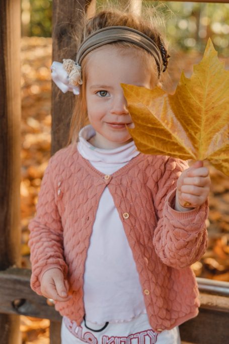 Ein kleines Mädchen mit Blume im Haar hält ein großes, orangefarbenes Blatt.