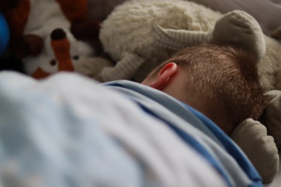 Ein schlafendes Kind mit Teddybären und Plüschtieren im Hintergrund.